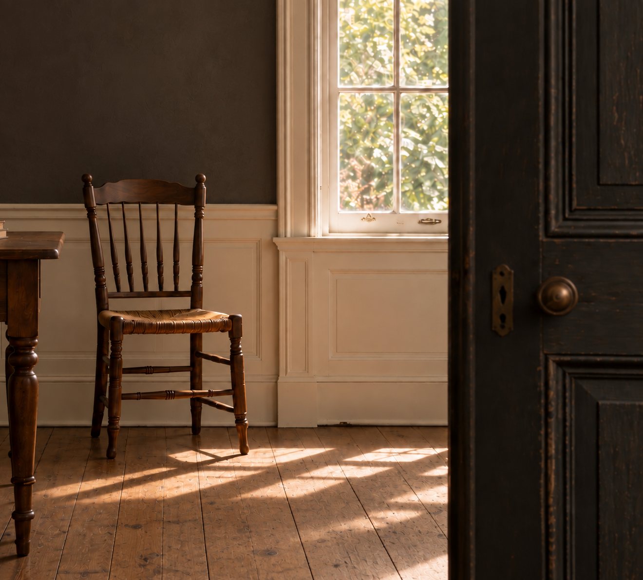 Sunlit room with an old wooden chair, dark brown wall and aged black door.